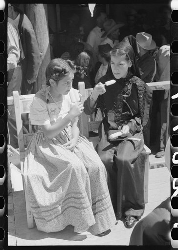 Two Spanish-American girls dressed in fiesta costumes eating popsicles, Taos, New Mexico