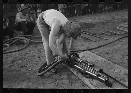 Miner attaching airhose to power drill which he will use in drilling contest, Labor Day celebration, Silverton, Colorado