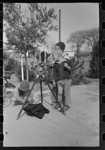 Children at the FSA (Farm Security Administration) Camelback Farms inspect the photographer's camera, Phoenix, Arizona