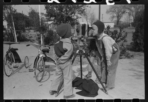 Children at the FSA (Farm Security Administration) Camelback Farms inspect the photographer's camera, Phoenix, Arizona