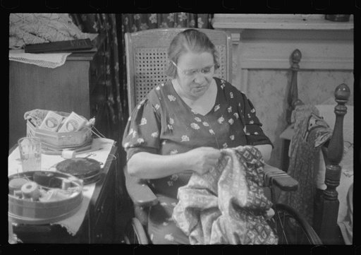 Washington, D.C. A woman doing handwork in her bedroom. Some hand-crochet work is lying on a dresser back of her and also in a work basket beside her