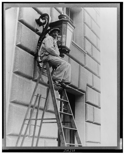 Washington, D.C. A government laborer on a stepladder cleaning a lamp above the entrance of the Commerce(?) building