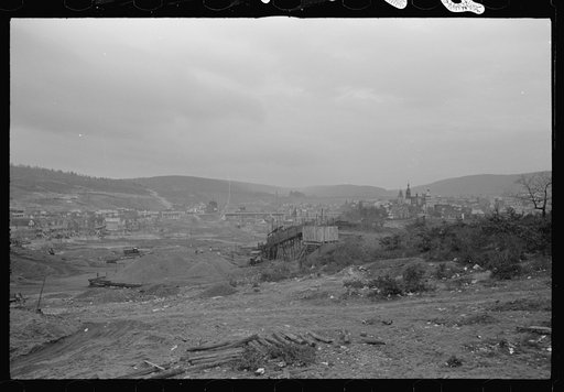 Mount Carmel,] Pennsylvania. A bird's-eye view of the town showing two sections, one showing big buildings and numerous church spires, and the other, rows of homes, connected by a bridge. Coalyards on the outskirts fill the foreground, and hills loom above the village, in the background of the pictu