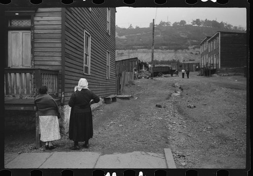 Shenandoah(?), Pennsylvania. Two women talking outside a house at the end of a street, watching some neighbors and the unloading of a truck on a drab-looking side street