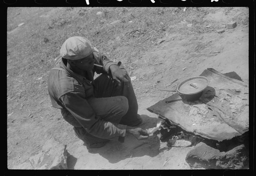 Migratory worker getting a light from the improvised stove over which he had cooked his lunch. Camden, North Carolina