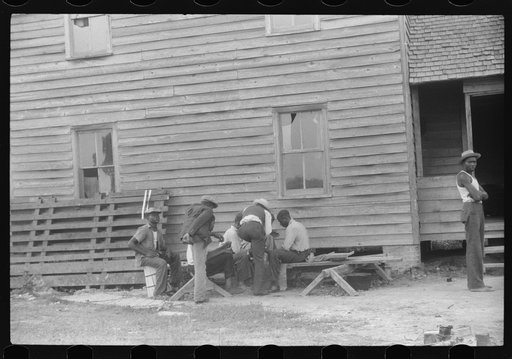Migratory agricultural workers playing cards while waiting for their truck to arrive. They are leaving today for another job at Onley, Virginia. Near Belcross, North Carolina