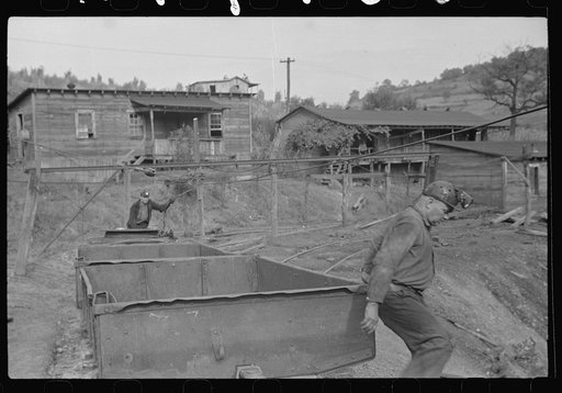 Miner lifting coal car on to track. Company houses in background. Chaplin, West Virginia