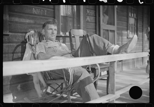 Untitled photo, possibly related to: Former coal miner sitting on his front porch. He is the town philosopher. He repairs his home (note railing and potato sack awning). Experiments with an elaborate garden on a hill about seven miles away. Jere, Scotts Run, West Virginia