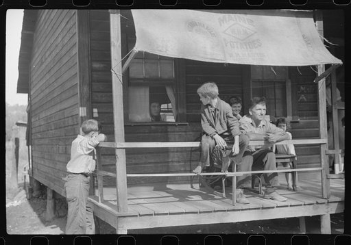 Untitled photo, possibly related to: Former coal miner sitting on his front porch. He is the town philosopher. He repairs his home (note railing and potato sack awning). Experiments with an elaborate garden on a hill about seven miles away. Jere, Scotts Run, West Virginia