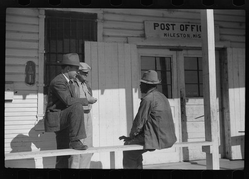 Mr. Jones, one of the owners of Marcella Plantation, with manager of Goodhope Plantation talking to one of Negro tenants on porch of Plantation store and post office, Mileston, Mississippi Delta, Mississippi