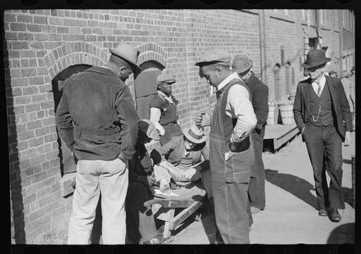 Farmer having corn removed from his foot on street outside tobacco warehouse during auction sales, Durham, North Carolina