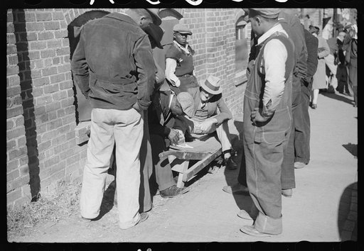 Farmer having corn removed from his foot on street outside tobacco warehouse during auction sales, Durham, North Carolina