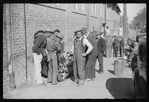 Untitled photo, possibly related to: Farmer having corn removed from his foot on street outside tobacco warehouse during auction sales, Durham, North Carolina