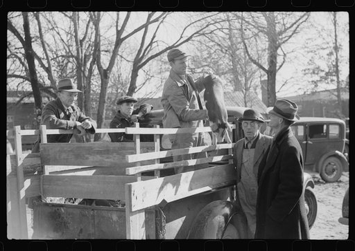 Farmer selling pig to other farmers outside warehouse. Many farmers bring livestock and supplies to sell to other farmers when they come to town with their tobacco for auction. Mebane, North Carolina