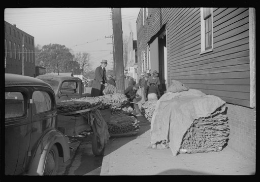 Farmers and warehousemen unloading tobacco on sidewalk, before auction sale. The warehouse was too overloaded to permit more tobacco being brought in. Mebane, North Carolina