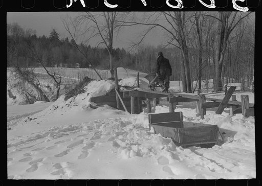 Hired man on Gilbert farm emptying load of manure after cleaning out the dairy barn early on a winter morning. Woodstock, Vermont