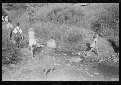 Children going home from school up Frozen Creek carrying their lunch pails. School is held in the summer and stops in January because the creek beds, roads and inadequate clothing make it impossible for them to come in severe weather. Breathitt County, Kentucky