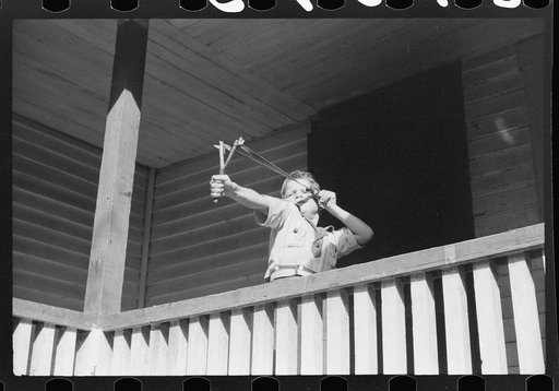 Mountain child shooting slingshot from porch of his home. Near Buckhorn, Kentucky