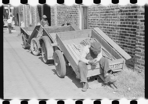 Farmers' trailers with tobacco sticks outside of warehouse during auction sale. Danville, Virginia