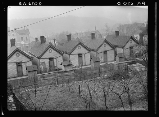 Row of identical houses off Eastern Avenue, in Cincinnati, Ohio, showing backyard outhouses. Ohio River Valley is in the distance