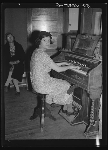 Wife of a resettled farmer playing organ at meeting of the Falls City Farmsteads Cooperative, Nebraska