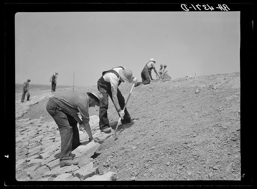 Laying stone on the face of a stock water dam. Pine Ridge land use project. Sioux County, Nebraska