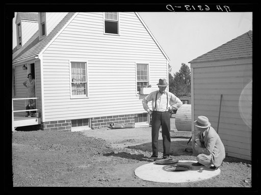 The Resettlement Administration community manager explains the operation of the sanitary underground automatic electric water pump and well to homesteader Langman. Granger, Iowa