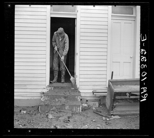 Man sweeping mud off the front steps of his house after flood. Posey County, Indiana