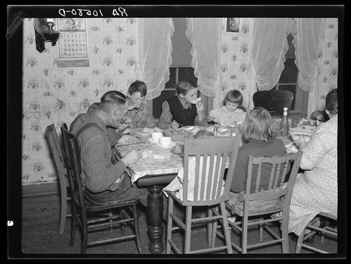 7:10 p.m. Tip Estes and family eating dinner. The day's work has been finished. Tip Estes has washed up and dinner is served