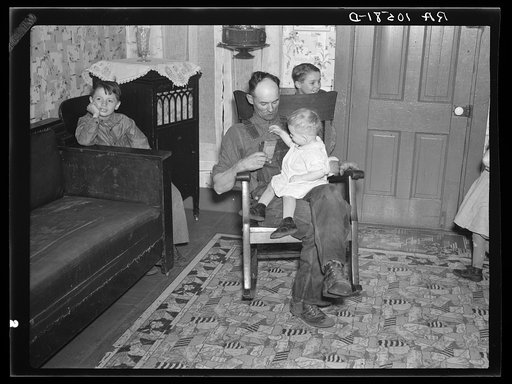 7:40 p.m. Tip Estes, hired man, with the youngest of his nine children. After dinner the family sits around until 8:00 or 8:30, when they go to bed. There is no reading matter in the house