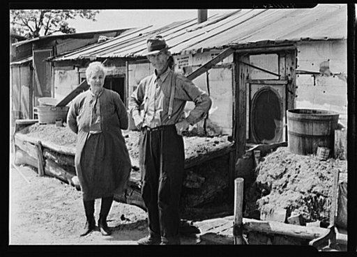 Mr. and  Mrs. Thompson standing in front of their log and peat cabin.  Thompson reckoned that he had had three crops out of nine on the land. Necedah project, Wisconsin