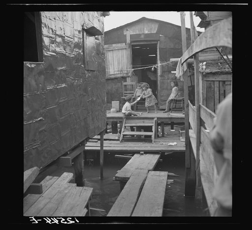 Children in the workers' quarter of Puerto de Tierra. Note the water of the tidal swamp under the houses and "sidewalk." San Juan, Puerto Rico