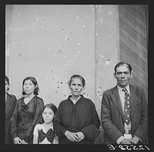 Families of Nationalist demonstrators who were killed in the Ponce massacre, standing before the Nationalist headquarters. Note machine gun bullets in wall. Ponce, Puerto Rico