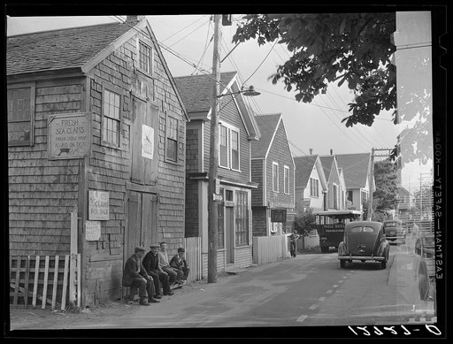 Commercial Street, the main street of Provincetown which runs along the waterfront, including a view of the "Sand Bar Club" and the tourist bus which runs out to the beach. Provincetown, Massachusetts