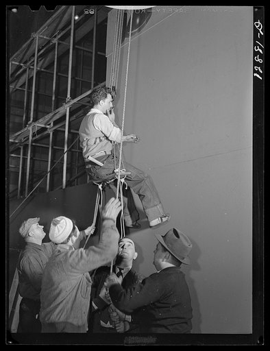 New York, New York. Installing the defense bond sales photomural, prepared by  the Farm Security Administration, in the concourse of the Grand Central terminal. Man ready to be hoisted in bo'sun's chair to make minor repairs and adjustments