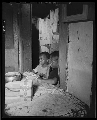Washington, D.C. Three children waiting in the kitchen while their mother prepares the evening meal