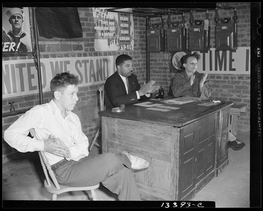 Washington, D.C. Air raid wardens' meeting in zone nine, Southwest area. Chairman, secretary and a messenger applauding a warden's report. Sidney Goldstein, the messenger, is the son of the neighborhood grocer