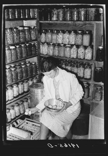 Mrs. Richard R. Gill, Donley County, Texas, prepares eggs for the market. The large containers are filled with homemade lard for this work grant family. Note that Mrs. Gill's attractive jacket is made from a sugar sack