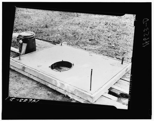 Concrete slab for sanitary privy. The stool at the left bolts on to the collar. The building is fastened to metal strips at corners. Minnesota
