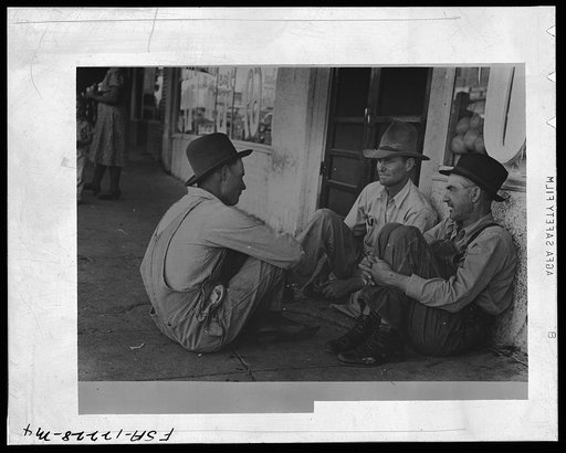 Farmers sitting aginst wall and squatting on sidewalk. Spur, Texas