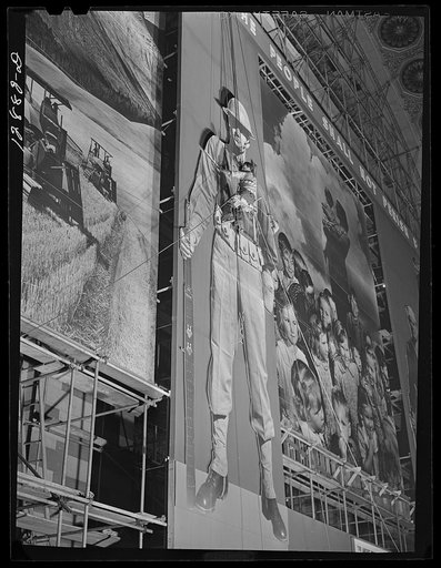 New York, New York. Installing the defense bond sales photomural, prepared by the Farm Security Administration, in the concourse  of the Grand Central terminal. Man on bo'sun's chair installing top section of one of the large figures