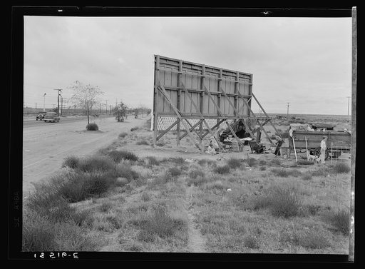 Untitled photo, possibly related to: Three families camped on the plains along U.S. 99 in California. They are camped behind a billboard which serves as a partial windbreak. All are in need of work