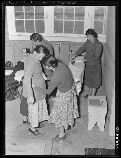 Camper receives help in fitting a coat from Works Progress Administration (WPA) sewing instructor. Shafter camp for migratory agricultural workers (Farm Security Administration-FSA), California