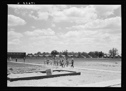 Tulare County, California. Farm Security Administration (FSA) camp for migrant agricultural workers. Nursery school children. Row of prefabricated steel shelters in which their families live shown in background