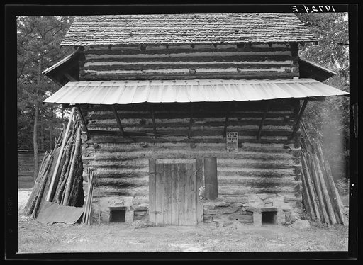 Untitled photo, possibly related to: Tobacco barn. Person County, North Carolina. Piece of sheet iron on the left is used to cover the opening of the furnace when starting the fire