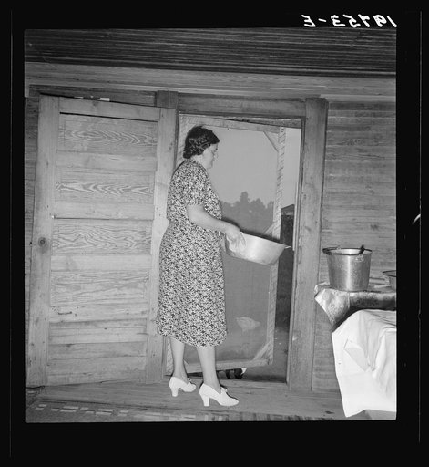 Tobacco sharecropper's wife disposing of dishwater after washing breakfast dishes. She put on white shoes for the photograph. Person County, North Carolina