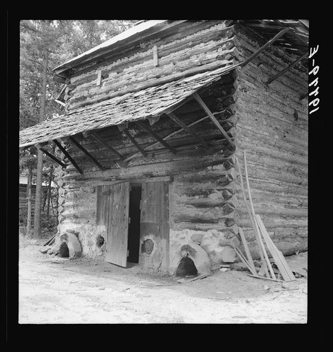 Tobacco barn with newly plastered furnace in preparation for "putting in."  Note main roof of tin and shelter roof of shingles. Person County, North Carolina