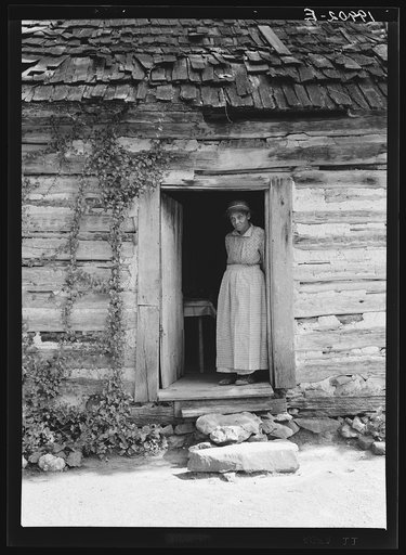Caroline Atwater standing in the kitchen doorway of double one and a half story log house. North Carolina