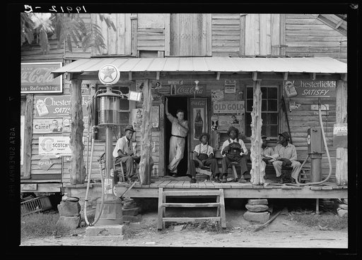 Untitled photo, possibly related to: Country store on dirt road. Sunday afternoon. Note the kerosene pump on the right and the gasoline pump on the left. Rough, unfinished timber posts have been used as supports for porch roof.  Negro men are sitting on the porch. Brother of store owner stands in do