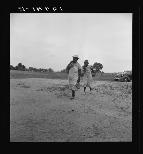 Mother of sharecropper family and friend coming up the road in the rain, bringing home sacks of vegetables from the neighbor place. Person County, North Carolina. Off Highway 144